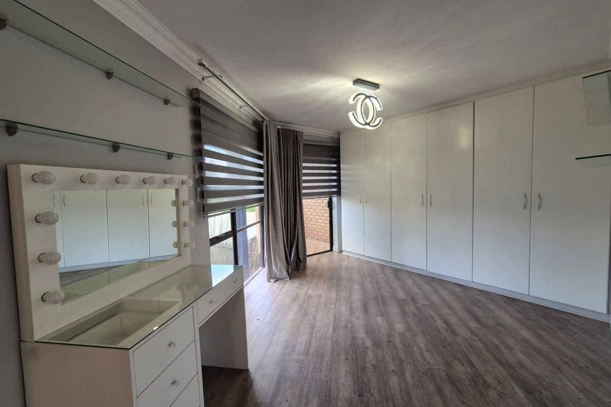 Spacious bedroom featuring extensive built-in cupboards, modern laminate flooring, and large windows with fitted roller blinds.
