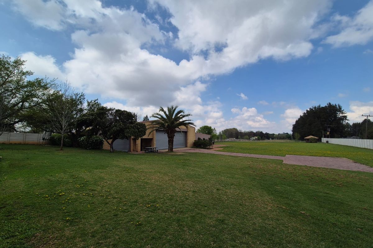 A spacious rear garden area featuring a large lawn, brick paved pathways, and access to the property's garage structure.