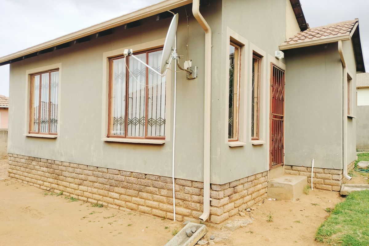 Rear exterior view of the house featuring a brick plinth, security gates, and installed satellite dish with standard guttering system.