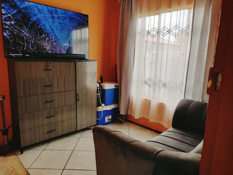 A living room area featuring tiled flooring and a window with curtains, providing natural light to the space.