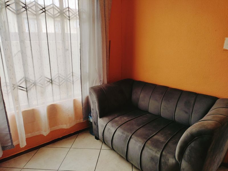 A living area featuring tiled flooring and a window fitted with a security gate, finished with bright orange wall paint.