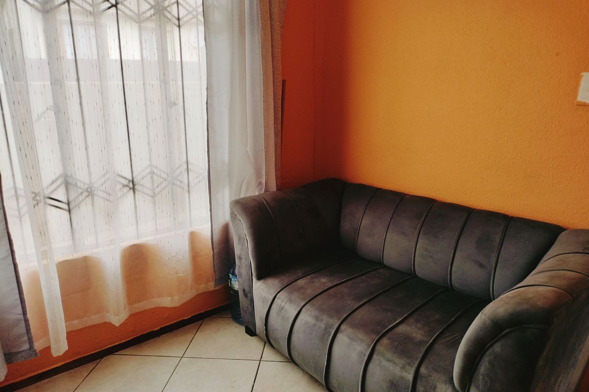 A living area featuring tiled flooring and a window fitted with a security gate, finished with bright orange wall paint.