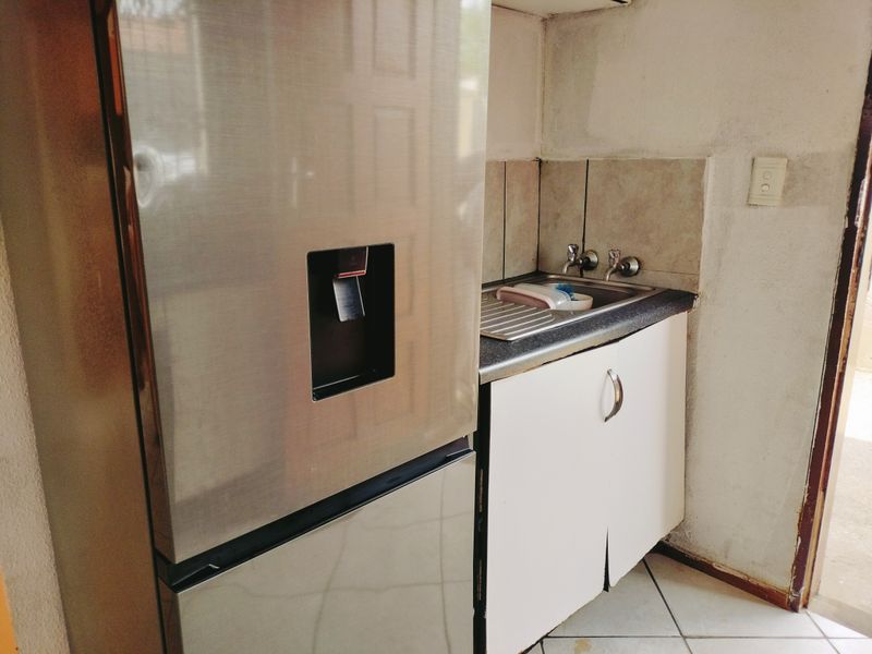 A compact scullery area featuring a stainless steel sink, tiled splashback, and built-in cabinetry with laminate countertops.