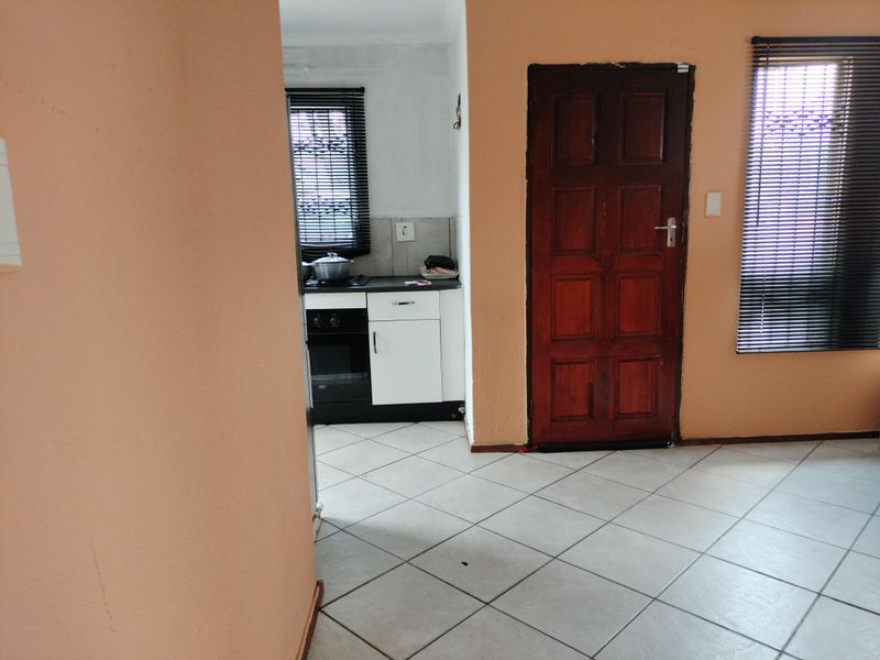 Open plan living area featuring tiled flooring, a compact kitchen with built-in oven and hob, and direct access via a solid timber door.