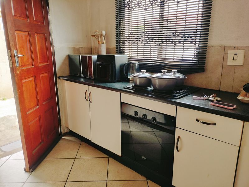 A functional kitchen area featuring built-in oven and hob, tiled flooring, and cabinetry with a tiled backsplash.