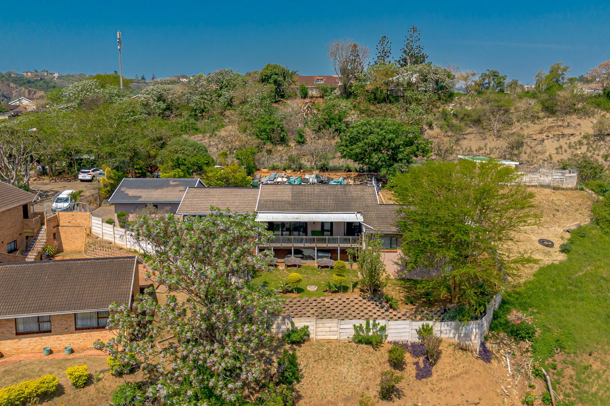 Aerial view of the property showcasing the main dwelling, tiled roof, balcony, and surrounding landscaped garden with boundary walls.