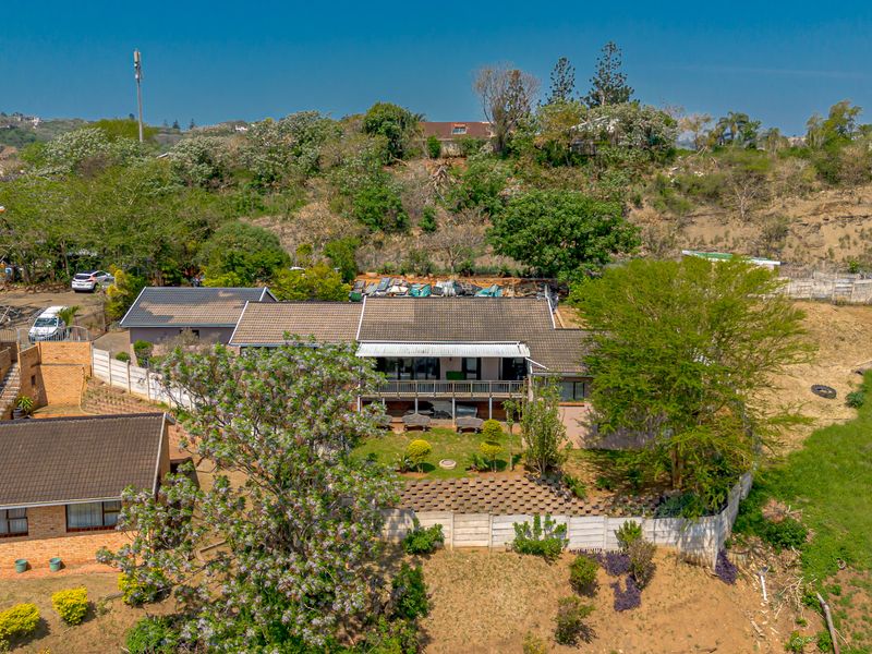 Aerial view of the property showcasing the main dwelling, tiled roof, balcony, and surrounding landscaped garden with boundary walls.