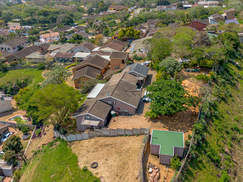 Aerial view of a residential property featuring a tiled roof house, an outbuilding, and a large garden area situated in a suburban neighborhood.
