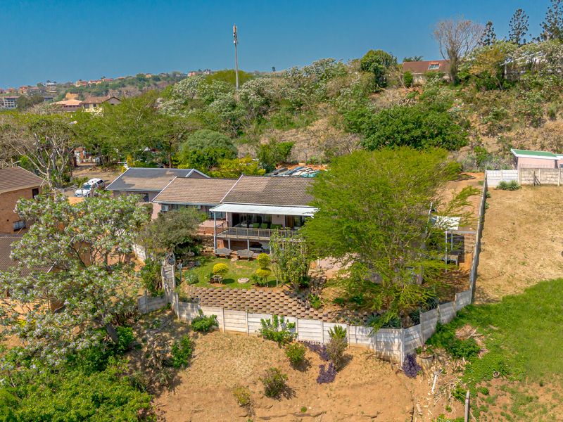 Aerial view of a residential property featuring a tiled roof house, covered patio, and landscaped garden area enclosed by concrete boundary walls.