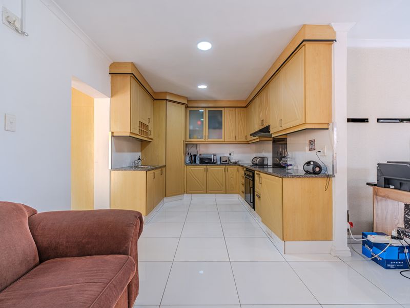 A functional kitchen featuring light wood cabinetry, granite countertops, integrated oven, extractor fan, and clean tiled flooring.