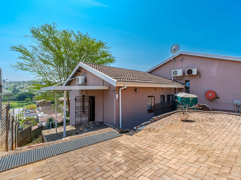 Rear exterior view of the property featuring a paved patio area, security gate, and wall-mounted air conditioning units.