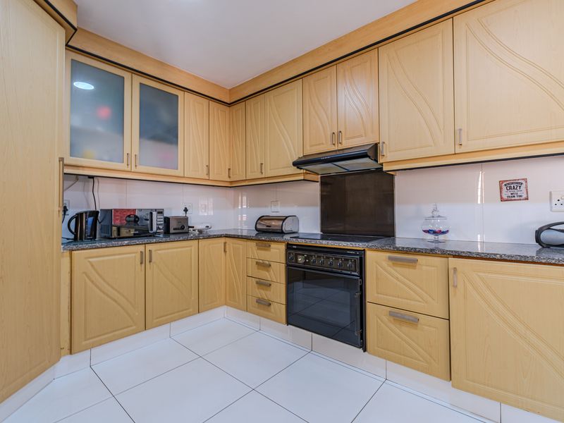 A functional kitchen featuring light wood-tone cabinetry, granite countertops, built-in oven, extractor fan, and clean white tiled flooring.