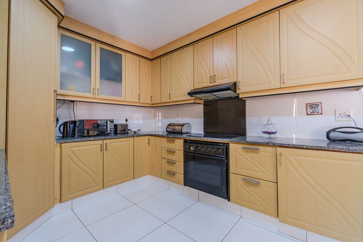 A functional kitchen featuring light wood-tone cabinetry, granite countertops, built-in oven, extractor fan, and clean white tiled flooring.