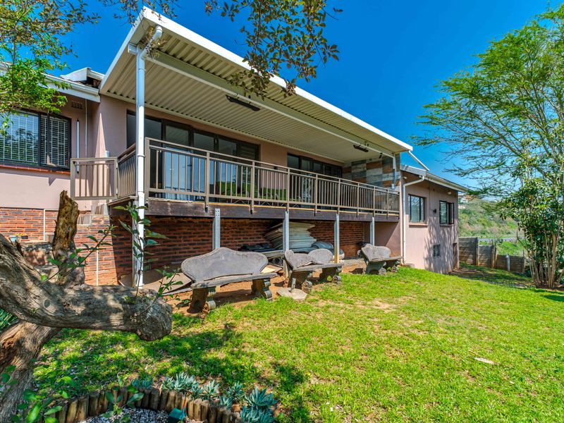 Rear view of the property featuring a raised wooden deck with metal balustrades, covered patio area, and access to the garden via sliding doors.