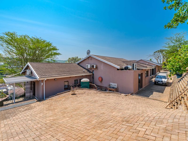 Rear view of the property featuring a paved driveway, tiled roof, and retaining wall structure with external utility fixtures.