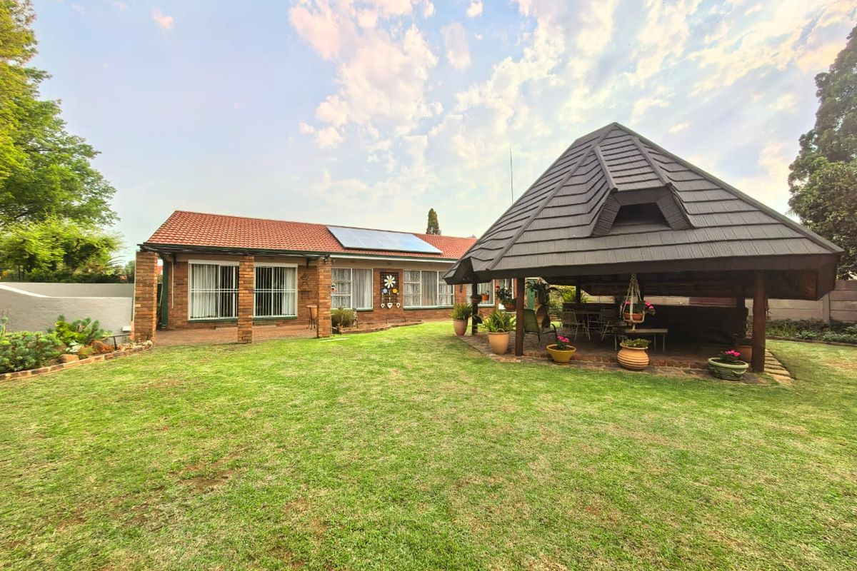 Spacious rear garden featuring a well-maintained lawn, brick-built house with solar panels, and a large covered gazebo area perfect for outdoor entertaining.
