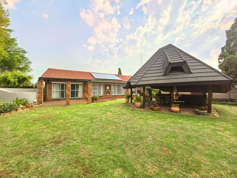 Spacious rear garden featuring a well-maintained lawn, brick-built house with solar panels, and a large covered gazebo area perfect for outdoor entertaining.