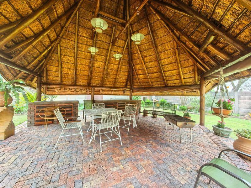 A spacious outdoor lapa area featuring a traditional thatched roof, exposed timber structure, brick paving, and a built-in brick bar counter.