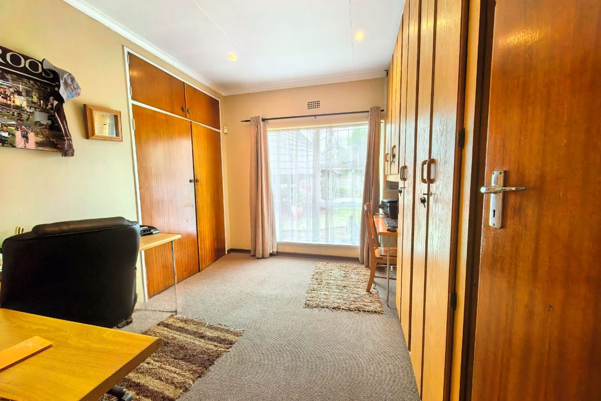 A bedroom featuring extensive built-in wooden cabinetry, carpeted flooring, and natural light from a window.
