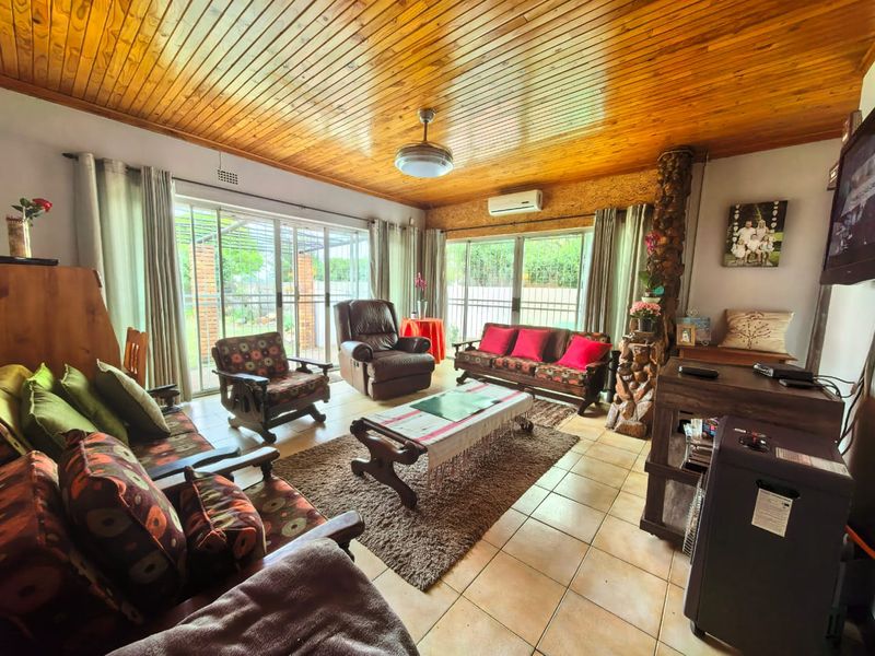 Spacious living room featuring a warm timber tongue and groove ceiling, ceramic tiled flooring, and large sliding glass doors providing access to the garden.
