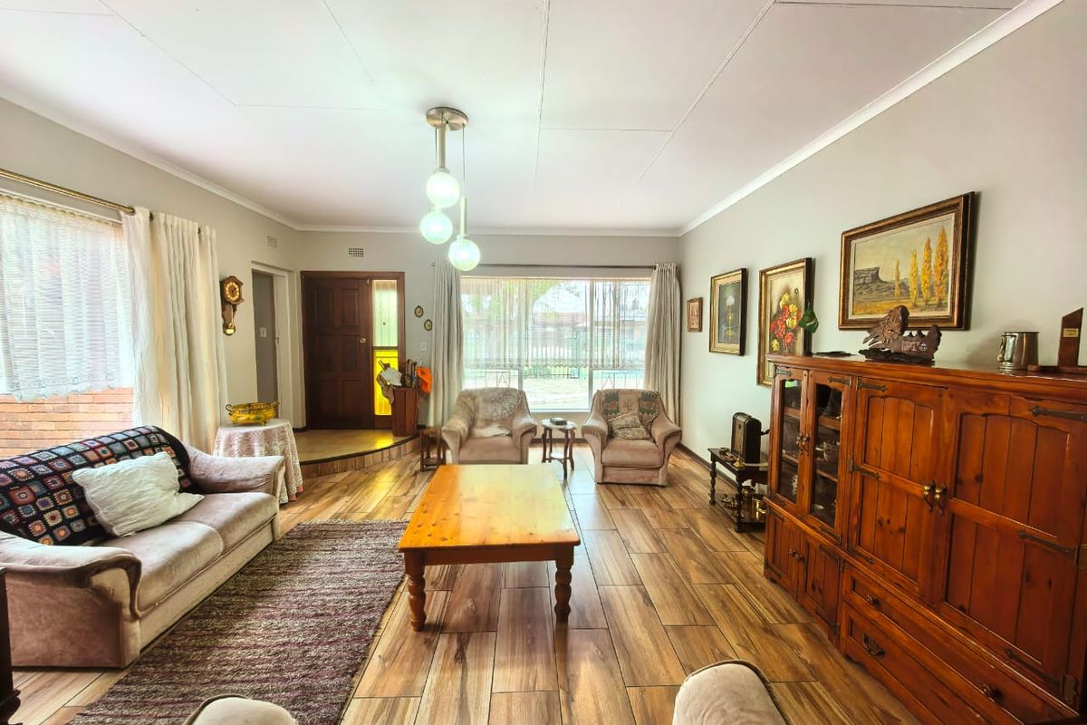 A spacious living room featuring wood-look tiled flooring, a large window providing natural light, and a classic timber entrance door.
