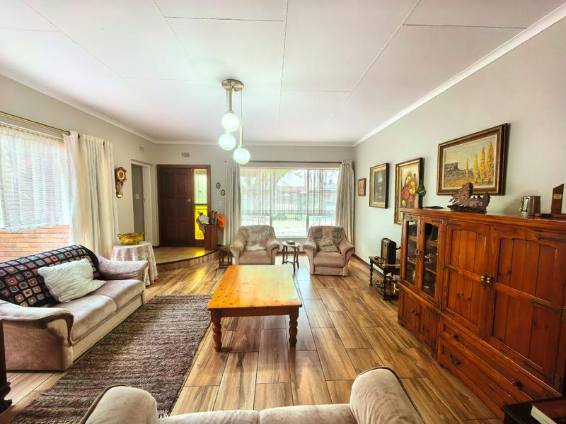 A spacious living room featuring wood-look tiled flooring, a large window providing natural light, and a classic timber entrance door.