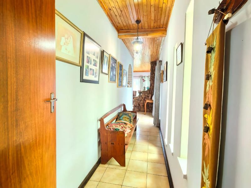 A long hallway featuring a warm timber tongue and groove ceiling, ceramic tiled flooring, and a solid timber door.