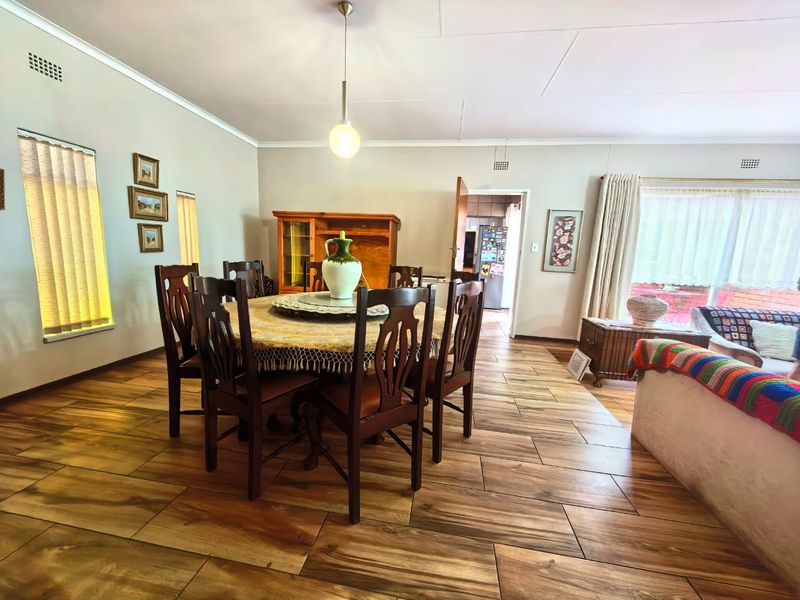 Open-plan dining and living area featuring wood-look tile flooring, neutral walls, and a central pendant light, with direct access to the kitchen.