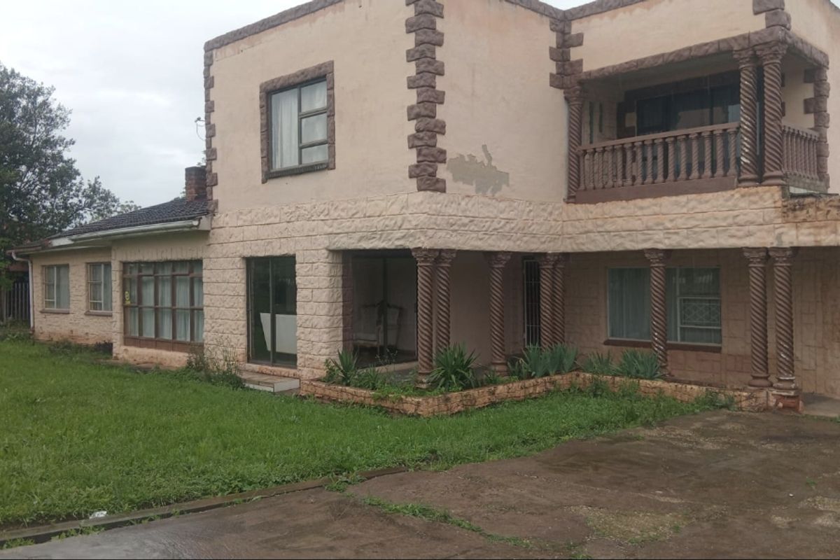 Two-story residential property featuring stone cladding, decorative columns, and a balcony, set on a large lot with a paved driveway and lawn area.