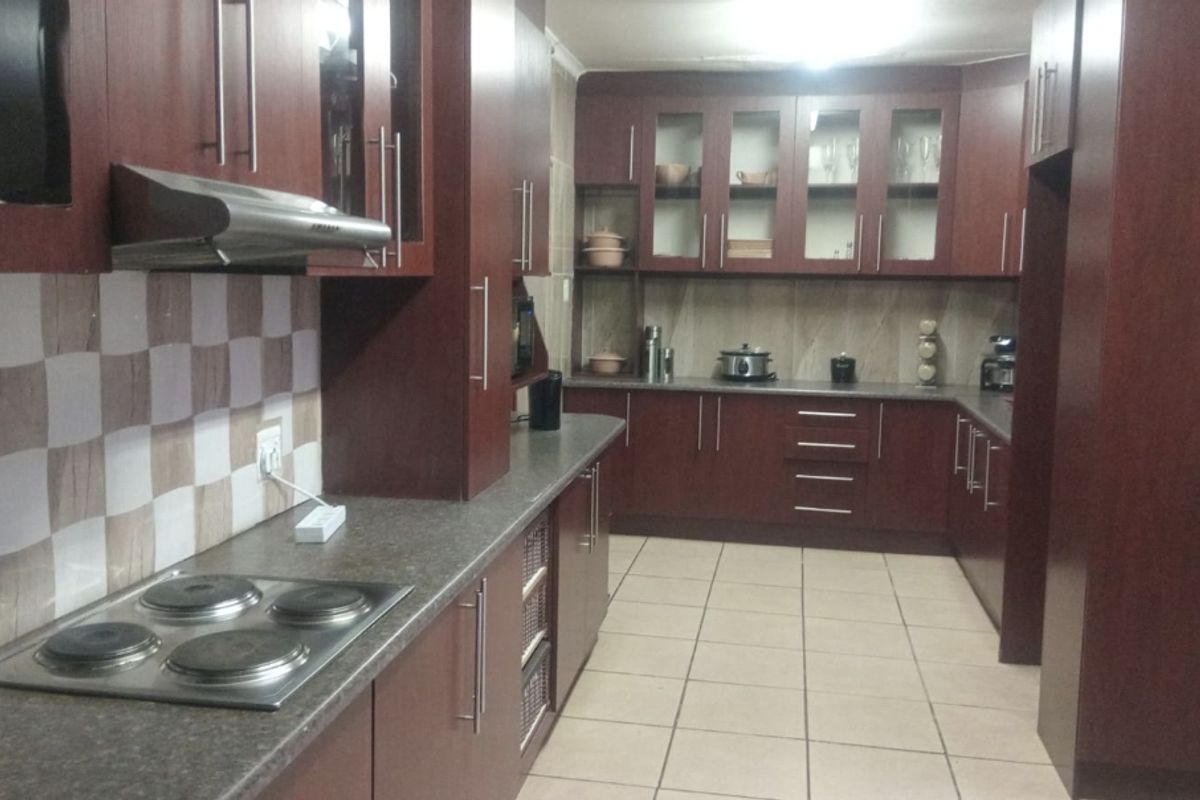 A functional kitchen featuring dark wood cabinetry, laminate countertops, an electric hob with extractor fan, and tiled flooring.