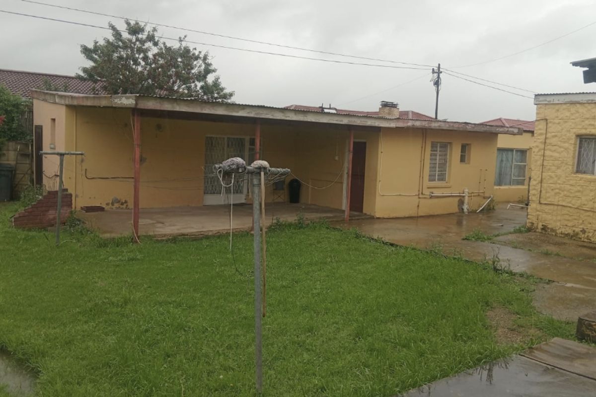 Rear view of the property featuring a covered patio area, concrete paving, and a spacious backyard with established lawn.