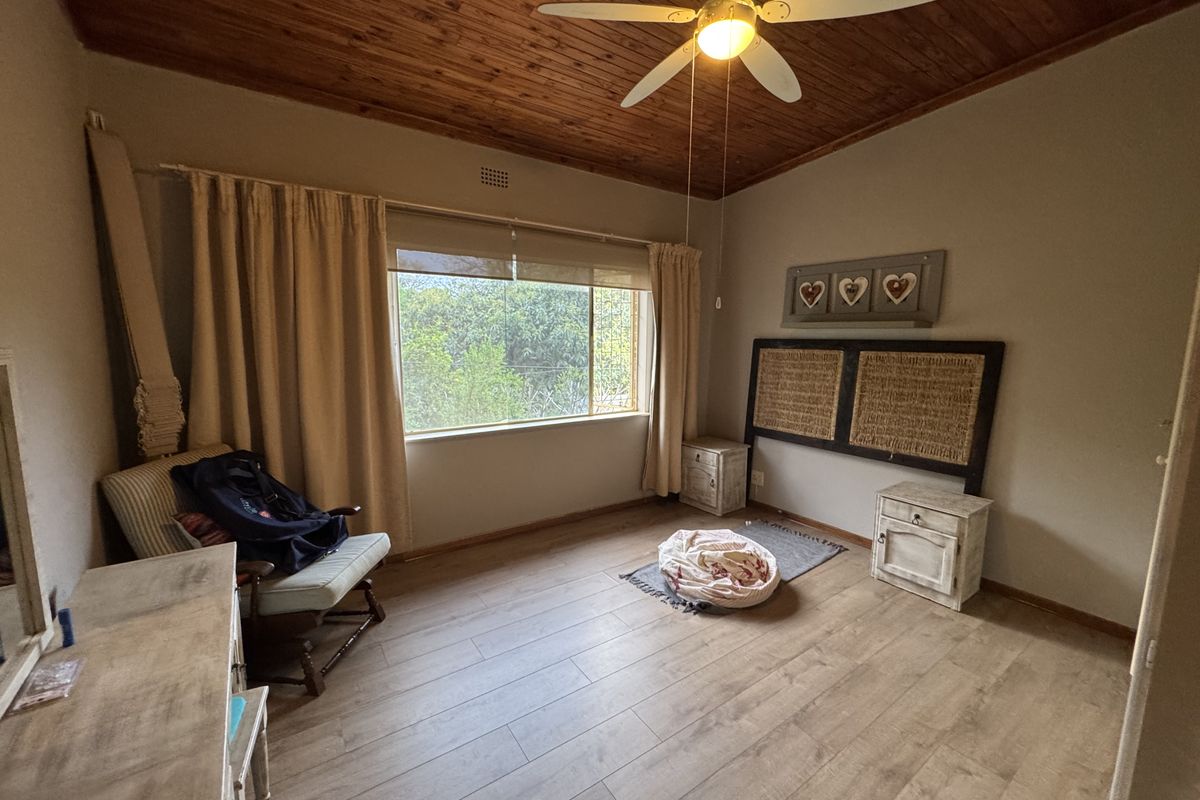 A bedroom featuring a warm timber ceiling, ceiling fan, and light-toned laminate flooring, offering a comfortable and functional living space.