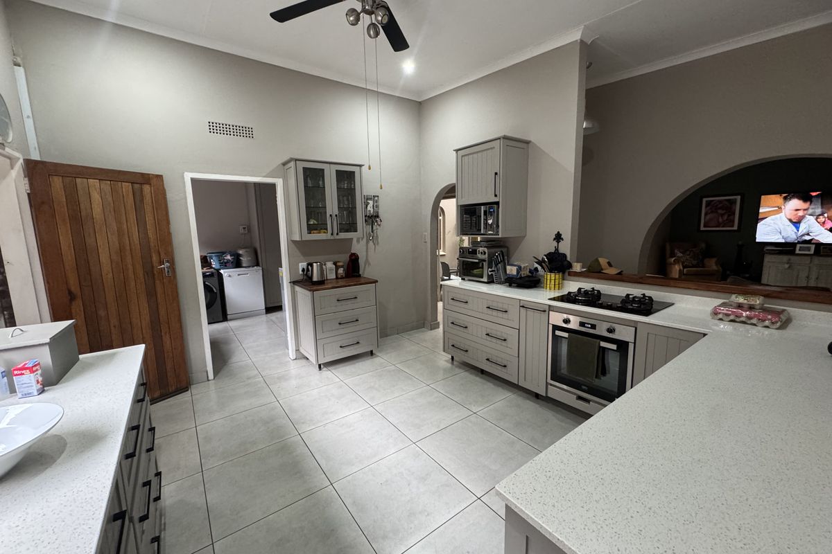 A well-maintained kitchen featuring light grey cabinetry, stone countertops, built-in oven, gas hob, and tiled flooring, with an open-plan flow to the living area.