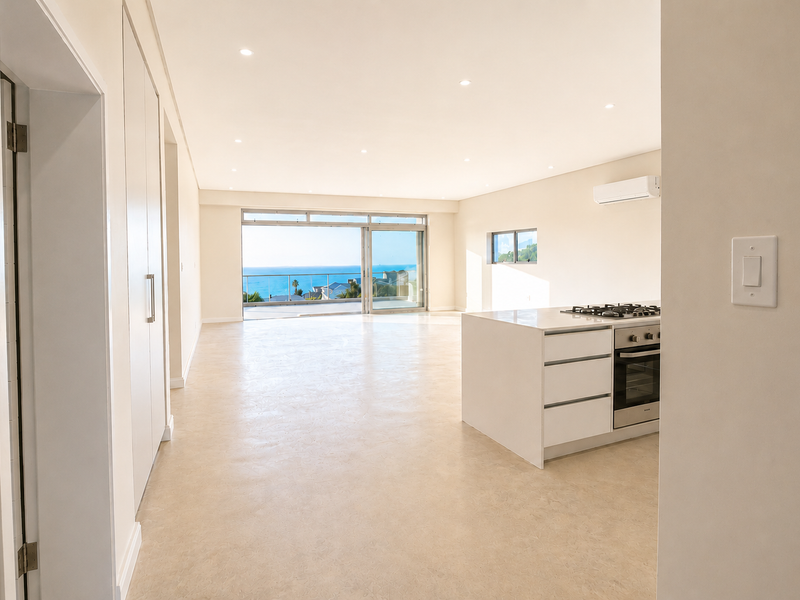 Spacious open-plan living area featuring a modern kitchen island with built-in appliances, recessed lighting, and large sliding doors opening to a scenic balcony.