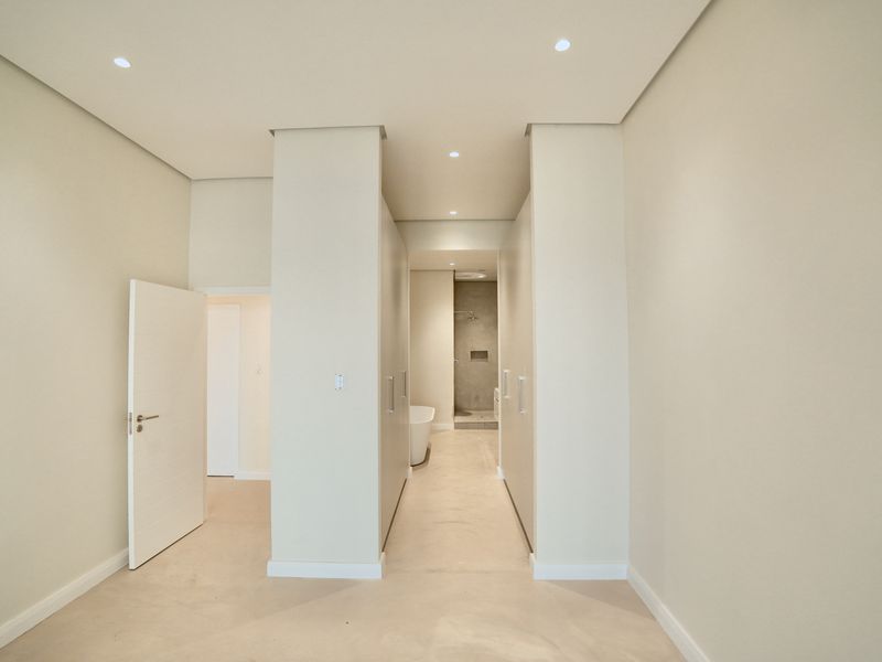 A modern, minimalist bathroom featuring a walk-in shower, freestanding bathtub, and integrated cabinetry with clean, neutral finishes.