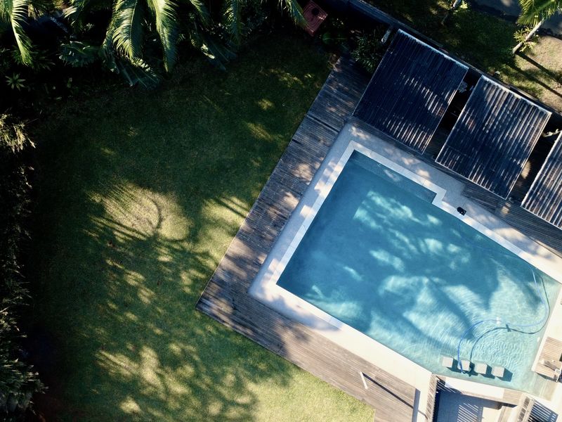 Aerial view of a private swimming pool surrounded by timber decking and lush garden landscaping.