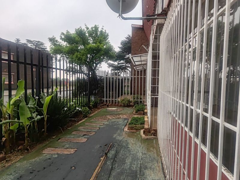 A narrow rear exterior walkway featuring security bars on windows, a satellite dish, and worn ground surfacing along the building perimeter.