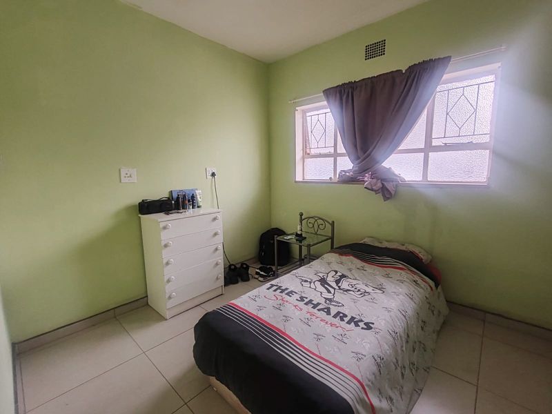A compact bedroom featuring tiled flooring and a metal-framed window with natural light, providing a functional space ready for cosmetic updates.
