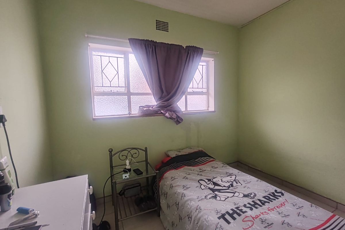 A compact bedroom featuring tiled flooring, a window with security bars, and a ventilation grille, requiring cosmetic updates to the wall finishes.