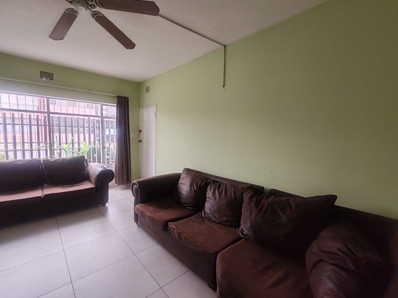 A living room featuring tiled flooring, a ceiling fan, and large windows. The space requires cosmetic updates to the wall finishes and electrical wiring.