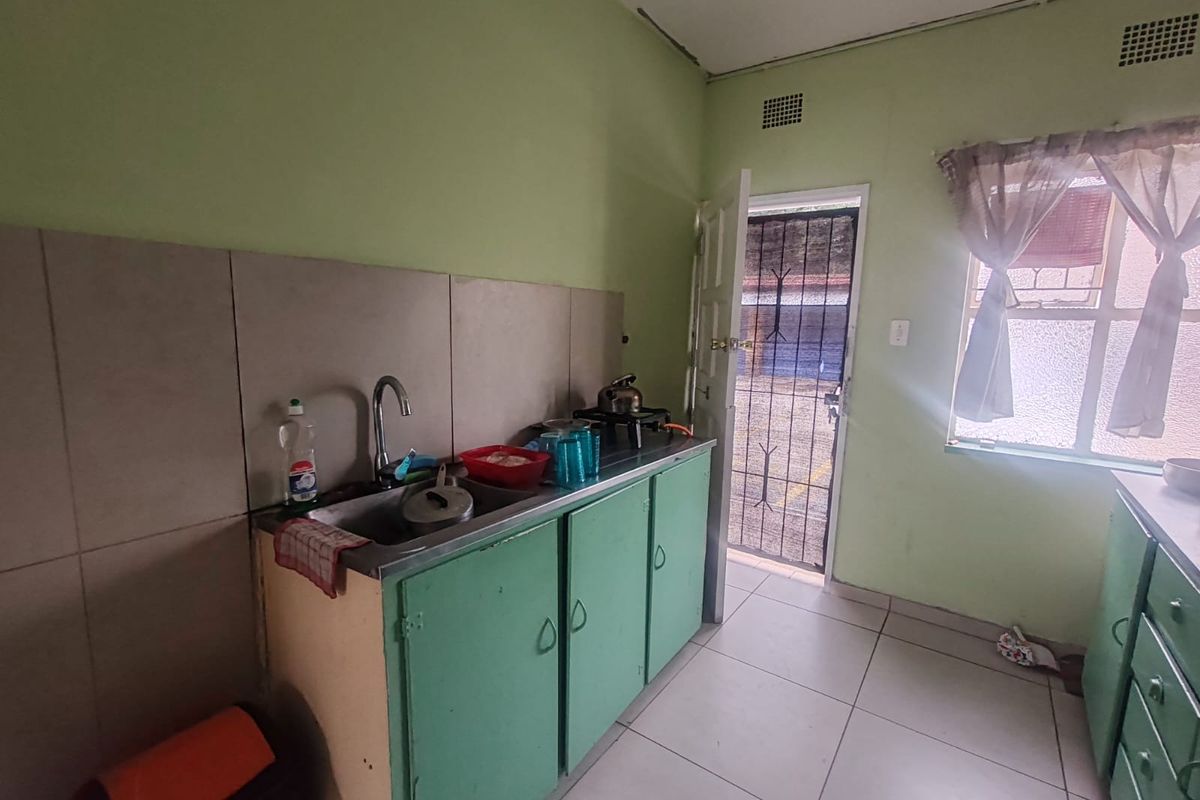 A functional kitchen featuring a stainless steel sink, tiled backsplash, and green cabinetry, with direct access to an exterior security gate.