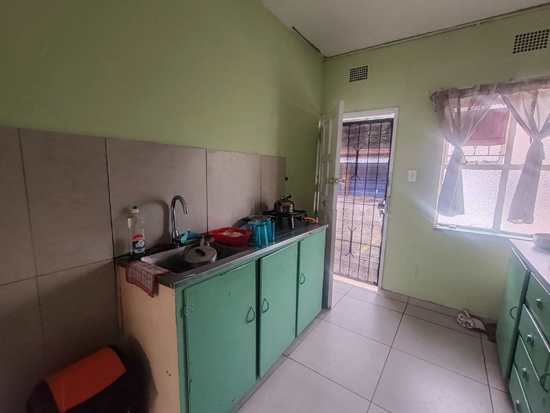 A functional kitchen featuring a stainless steel sink, tiled backsplash, and green cabinetry, with direct access to an exterior security gate.