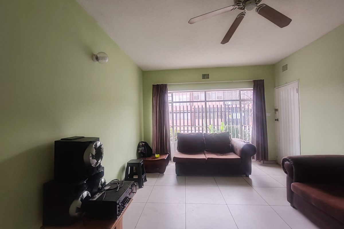 A living room featuring tiled flooring, a ceiling fan, and a large window with security bars, providing natural light to the space.