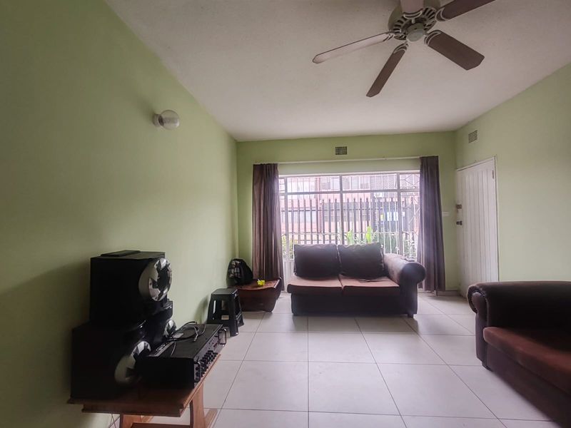 A living room featuring tiled flooring, a ceiling fan, and a large window with security bars, providing natural light to the space.