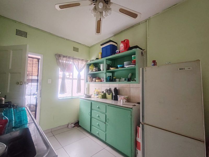 A functional kitchen featuring built-in cabinetry, tiled backsplash, and tiled flooring, offering potential for modernization and cosmetic updates.