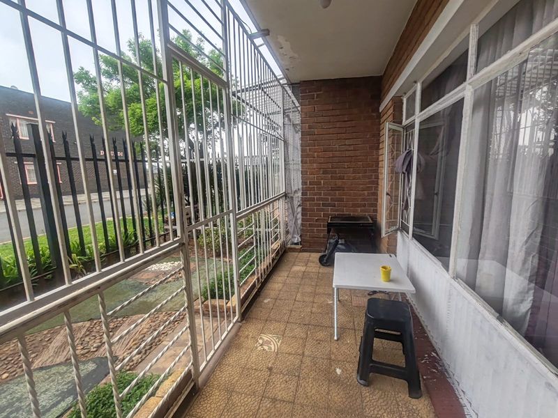 A covered balcony area featuring brick wall accents, tiled flooring, and a full-length security gate enclosure.