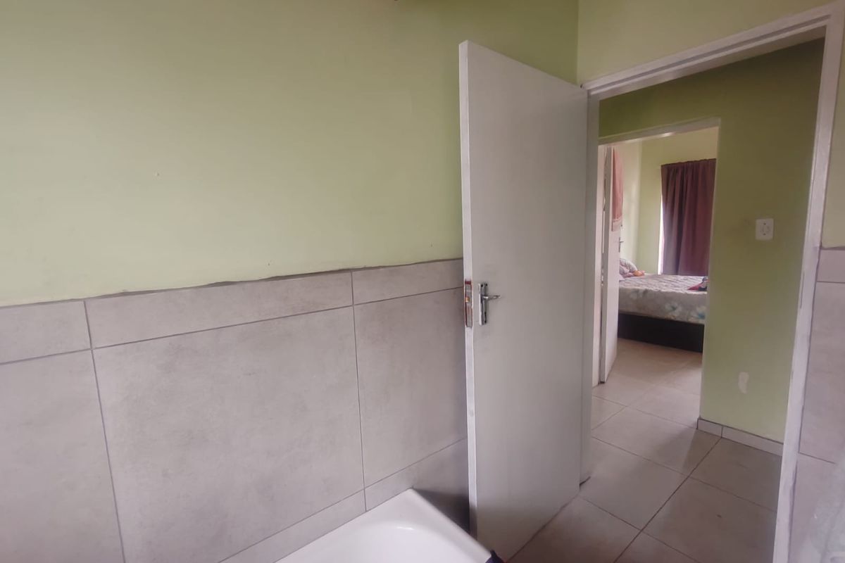 A functional bathroom space featuring a bathtub and partial wall tiling, with an adjacent view into a bedroom area.