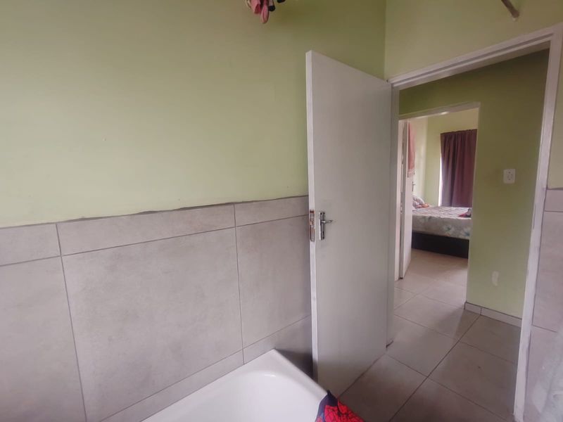 A functional bathroom space featuring a bathtub and partial wall tiling, with an adjacent view into a bedroom area.