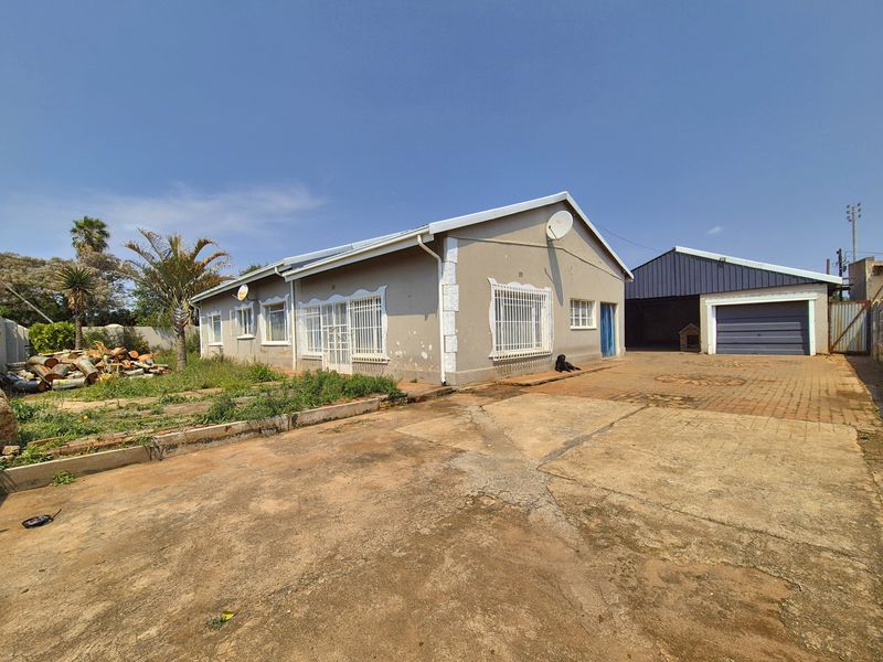 Front exterior view of a single-story house featuring a concrete driveway, security bars on windows, and a detached garage structure.