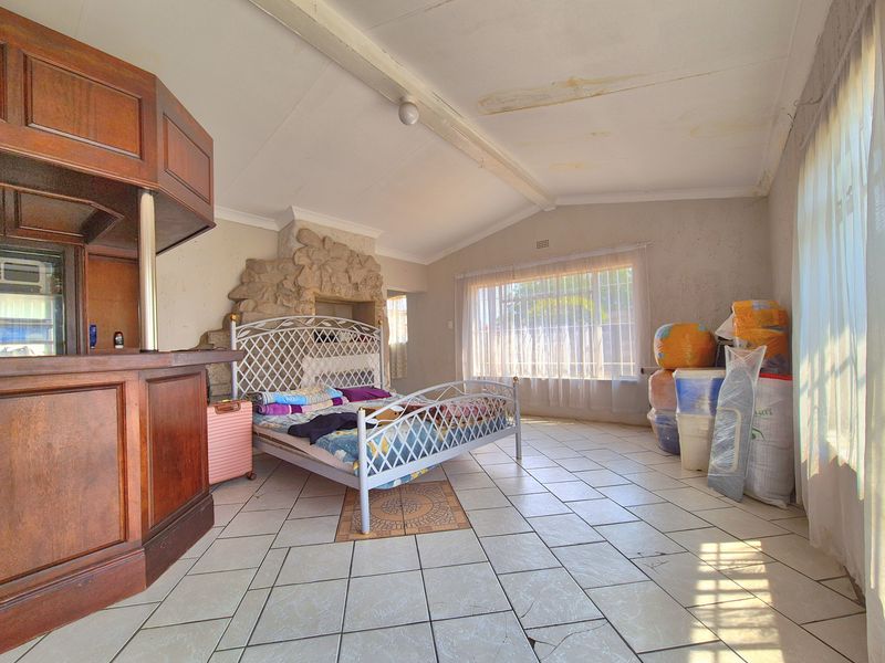 Spacious living area featuring a built-in bar, stone fireplace, and tiled flooring, offering potential for renovation and modernization.